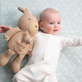 Baby holding a knitted teddy bear against a light blue background with subtle patterns