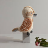 Knitted toy sloth on a wooden block with a minimal background