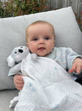 Baby lying on a gray cushion holding a white blanket and koala toy outdoors.