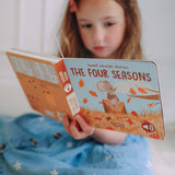 Child reading a book titled 'The Four Seasons' with a mouse illustration on the cover.