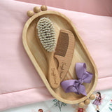 Close-up of Snuggle Hunny natural wooden baby hairbrush showing soft nylon bristles and engraved handle.