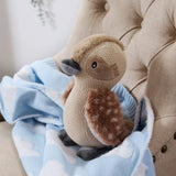 Plush duck toy on a blue and white blanket with a beige chair in the background