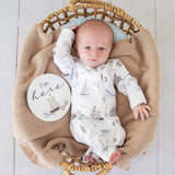 Baby in a wicker basket with a 'I'm here' sign on a light wooden floor.