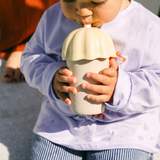 Child holding and drinking from a unique-shaped cup outdoors