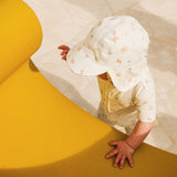 Child wearing a white sun hat and matching outfit on a yellow and white background