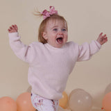 Child in a pink sweater with balloons in the background