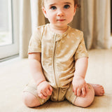 Baby wearing a beige onesie with a zipper sitting on a light-colored floor.