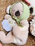Plush toy koala wearing a green hat on a woven surface with flowers.