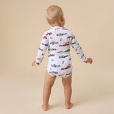 Child wearing a long-sleeve onesie with car pattern on a beige background