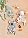 Three soft animal toys with rings on a beige surface, surrounded by greenery.