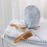 Baby grooming tools including a brush, comb, and mitt on a white surface with a striped towel.