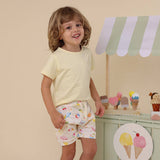 Child wearing a yellow shirt and patterned shorts standing in front of an ice cream-themed play area.