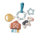 A baby teething ring toy with multiple soft and hard accessories, including a blue fabric ring, a light blue star teether, a beige sun-shaped teether, a cow plush, and a barn plush, on a white background.