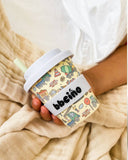 Person holding a colorful cup with 'bbeino' branding against a beige blanket background