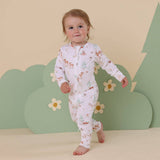 Child wearing a floral onesie against a green and beige background with flowers and trees.