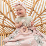 Baby sitting in a wicker chair holding a toy, wrapped in a pink blanket with elephant patterns.