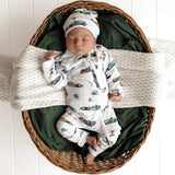 Newborn baby in a car-themed outfit lying in a woven basket with green and white blankets.