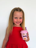 Young girl in a red dress holding a pink cup with a straw against a white background
