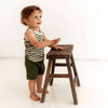 Child standing next to a wooden stool on a white background