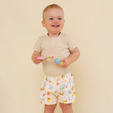 Child wearing a beige shirt and patterned shorts holding toys against a beige background