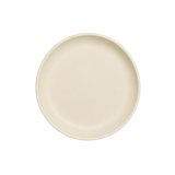 A minimalist round ceramic plate in a warm cream or off-white color, photographed from directly above on a solid white background.