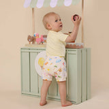 Baby wearing a diaper with a colorful design, standing in front of a green cabinet.