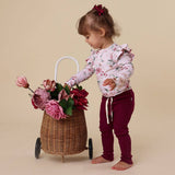Child with a floral outfit standing next to a basket of flowers on a beige background