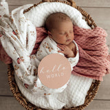 Newborn baby wrapped in a floral blanket with 'hello world' text in a wooden basket.
