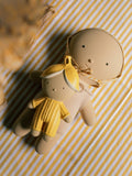 Two handmade clay dolls, one larger doll wearing a beige bonnet and the smaller doll in a yellow dress, resting on a yellow and white striped fabric background.