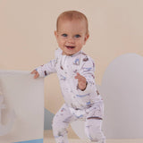 Baby in a white onesie with nautical patterns standing on a beige background