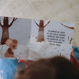 Child reading a winter-themed book with a mouse and snowman illustration.