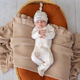 Newborn baby sleeping in a basket with a beige blanket and white hat.