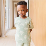 Child wearing a light green sweater with palm tree patterns indoors.