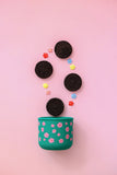 Green container with floral design on a pink background, containing Oreo cookies and decorative flowers.