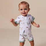A baby wearing a short-sleeve white zip-up romper with a woodland animal print and sage green trim, standing against a solid beige background.