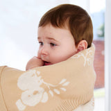Baby wrapped in a beige blanket with floral patterns, looking around.