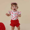 Child wearing a strawberry-patterned shirt and red shorts on a beige background