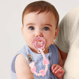Baby with a pink teething ring and pacifier held by an adult against a light background