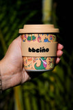 Hand holding a colorful coffee cup with 'bboiño' branding against a dark background