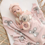 Baby wrapped in a pink blanket with koala designs, holding a koala toy.