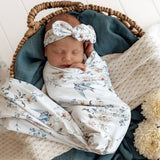 Newborn baby swaddled in a floral blanket with a matching headband, lying in a woven basket.