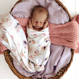 Newborn baby wrapped in a floral blanket in a wicker basket with pink and purple blankets.