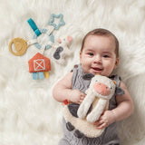 Baby holding a plush cow toy with colorful toys in the background on a white fluffy surface