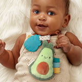 Baby holding a plush avocado toy with colorful accents on a soft white background