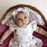 Baby in a floral outfit sitting in a wicker basket with a white background