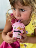 Child drinking from a pink cup with cartoon characters on it.