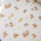 A close-up of a white fabric or paper surface printed with a repeating farm-themed pattern featuring brown pigs, yellow chicks, hay bales, small fences, and a few green leaves.