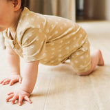 Baby in a beige outfit with white patterns crawling on a light-colored floor.