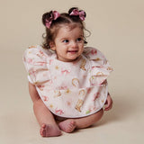 A baby girl wearing a white bib with a pink and gold western-themed print, sitting against a solid beige background.
