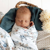 Newborn baby swaddled in a floral blanket, lying on a textured surface with a decorative flower.